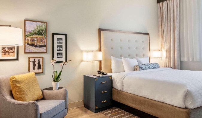 Kamar hotel yang cerah dengan seni di dinding, kursi malas, dan tempat tidur berukuran queen di St. Charles Coach House, sebuah hotel di New Orleans, Louisiana