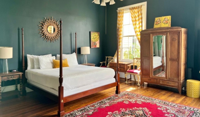 Kamar tamu dengan dinding hijau tua, lantai kayu keras, tempat tidur bertiang empat, lemari kayu, dan jendela besar di Creole Gardens Inn, sebuah hotel di New Orleans, Louisiana